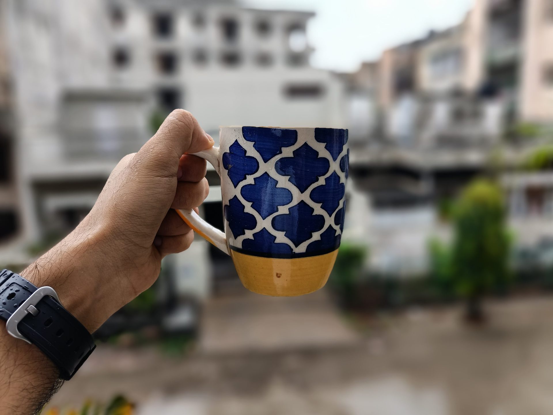 POCO F3 GT portrait mode from rear camerar POCO F3 GT portrait mode from rear camera of hand holding a colorful blue, white, and yellow mug in front of a window.